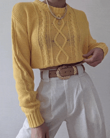 a woman wearing a yellow sweater and white pants has a belt around her waist