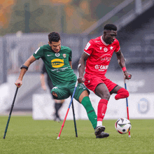 a man with crutches is playing soccer with a man in a green martini shirt