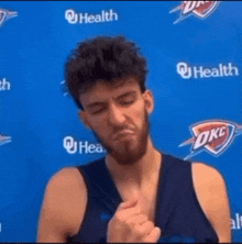 a man with a beard is standing in front of a blue wall with a okc logo on it .