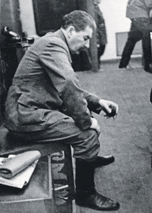 a black and white photo of a man sitting on a stool with his legs crossed