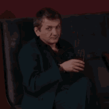 a man in a blue suit is sitting on a couch holding a glass