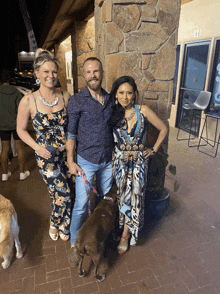 a man and two women standing next to a dog in front of a stone wall