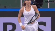 a woman in a white tank top is holding a tennis racquet ..