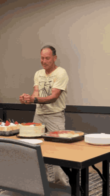 a man in a yellow shirt with a bicycle on it stands in front of a table with a cake on it