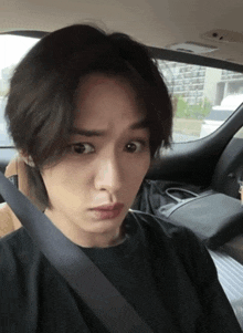 a young man wearing a black shirt is sitting in a car with a seat belt around his neck