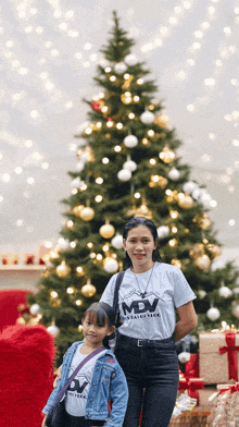 a woman and a girl are standing in front of a christmas tree .