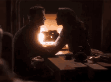 a man and a woman are sitting at a table holding hands and kissing in front of a fireplace .