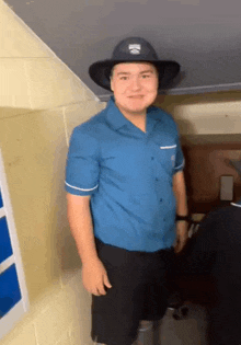 a man wearing a cowboy hat and a blue shirt stands in a hallway