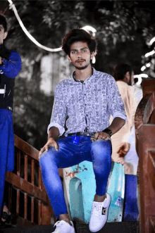 a young man wearing a white shirt and blue jeans sits on a stool