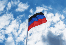 a red white and blue flag is waving in the wind against a cloudy blue sky