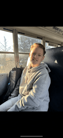 a young boy is sitting on a bus wearing a hoodie that says hypesquad