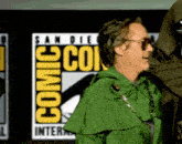 a man in a green cape is standing in front of a comic con logo