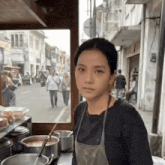 a woman wearing an apron is standing in front of pots and pans on a street