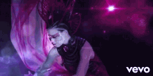 a woman in a purple dress is dancing in front of a purple background with the word vevo on the bottom .