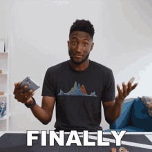 a man in a black shirt is holding a cell phone in front of a table that says finally on it