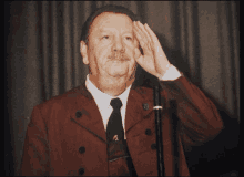 a man wearing a red jacket and a black tie salutes