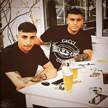 a man in a gucci shirt sits next to another man