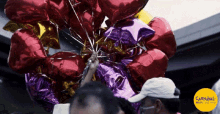 a bunch of red and purple balloons are being held by a man with a carnival logo on the bottom