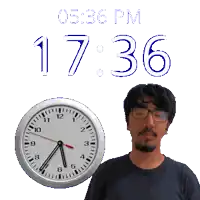 a man wearing glasses stands in front of a clock that says 1736