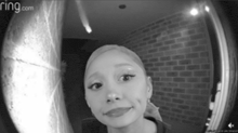 a black and white photo of a woman looking through a ring doorbell