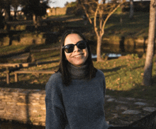 a woman wearing sunglasses and a turtleneck sweater smiles for the camera