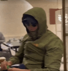 a man wearing a hooded jacket and sunglasses is sitting at a table