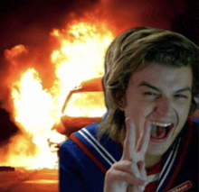 a young man giving a peace sign in front of a fire