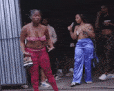 a group of women are standing in front of a building . one of the women is wearing a bra and blue pants .