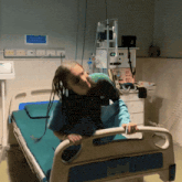 a woman with dreadlocks is sitting in a hospital bed with a monitor that says ' emergency ' on it