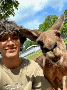 a man wearing a primitive shirt holds a kangaroo on his shoulder