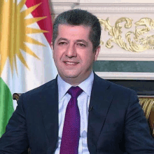 a man in a suit and tie is smiling in front of a kurdish flag .