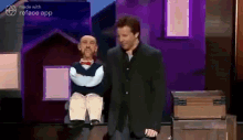 a man in a suit is standing next to a puppet .