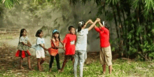 a group of children are standing in a circle holding hands in the grass .