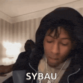 a man wearing headphones and a hooded jacket says sybau .