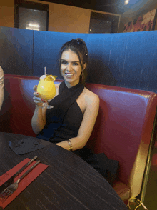 a woman in a black dress is holding a large yellow drink