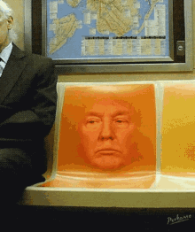 a man in a suit sits on a subway seat with a picture of donald trump behind him