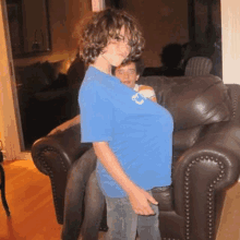 a boy in a blue shirt with the letter c on it is standing next to a couch