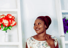 a woman wearing a turban smiles in front of a shelf of flowers