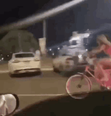 a woman is riding a bicycle down a street next to a car at night .