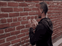 a man is standing in front of a brick wall and touching it with his hands