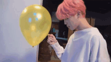 a man with pink hair is holding a yellow balloon .