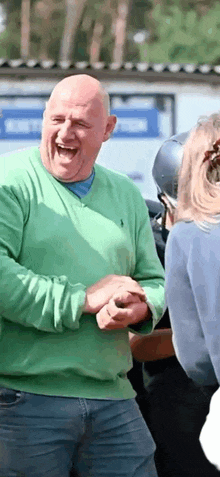 a bald man in a green sweater is laughing with a woman .