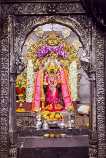 a statue of a woman in a pink dress is surrounded by flowers and offerings