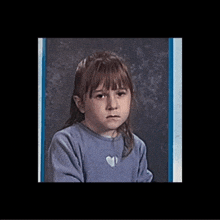 a little girl in a blue shirt with a heart necklace is making a sad face .