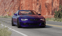 a purple car is driving down a road in front of a rock wall