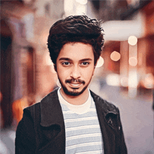 a young man with a beard is wearing a black jacket and striped shirt