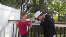 a boy wearing a red shirt with a spiderman on it is standing next to a boy wearing a white hat