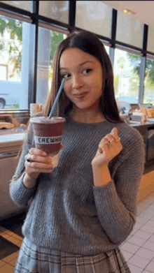 a woman in a gray sweater is holding a cup that says crew on it .