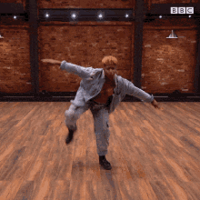 a man is dancing on a wooden floor in front of a brick wall and a sign that says bbc