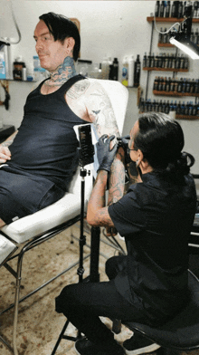 a man in a black tank top is getting a tattoo